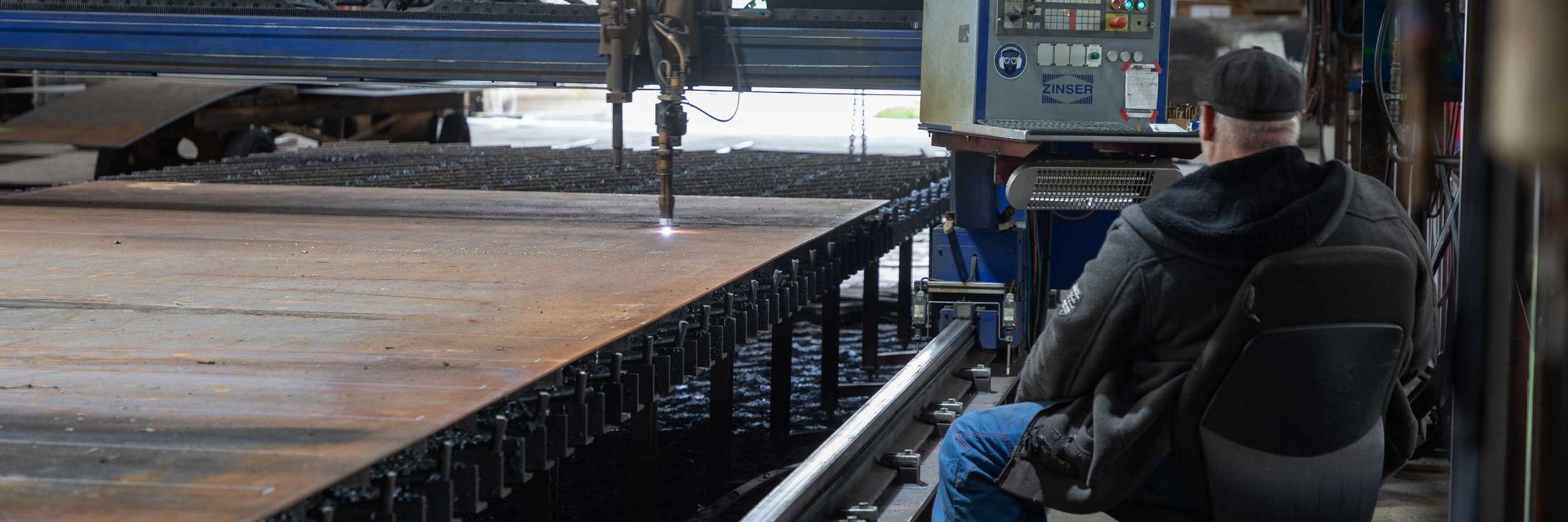 © Felbermayr/Weickinger Eine Maschine fräst Treile für den Schiffsbau. Ein Arbeiter kontrolliert die Arbeiten.