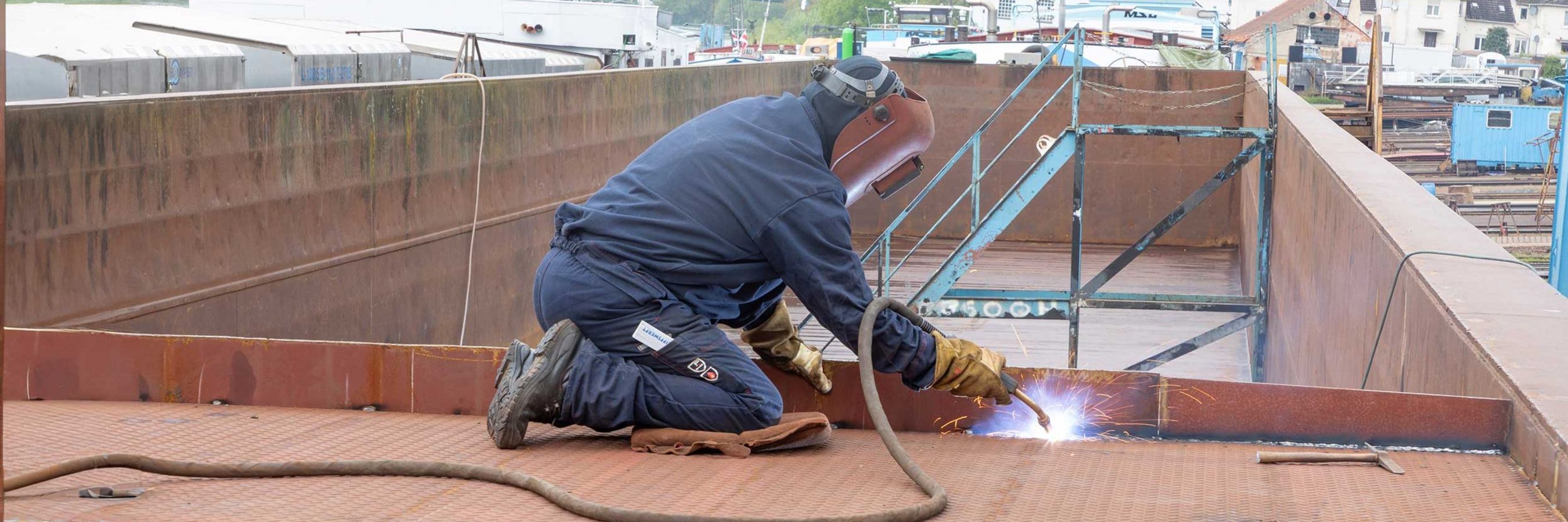 © Felbermayr/Weickinger Schweißer bei Schweißarbeiten kniet am Deck eines Schiffes.